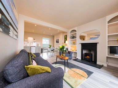 A living room with a gray sofa and armchair a fireplace and a dining area at Harbour View Cottage in Watchet