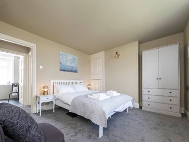A bedroom with a double bed bedside tables lamps a wardrobe and an open door to a bathroom at Harbour View Cottage in Watchet
