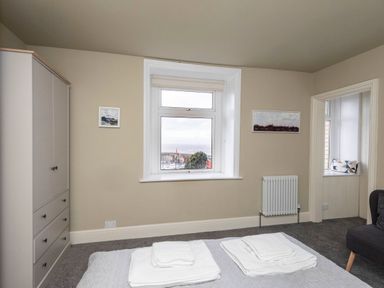 A bedroom with a bed, wardrobe, window showing sea view, radiator, and a small seating nook at Harbour View Cottage in Watchet