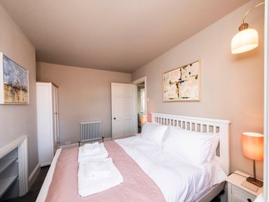 A bedroom with a white bed and pink bedding two folded towels two bedside tables lamps and wall art at Harbour View Cottage in Watchet