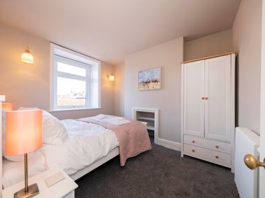 A bedroom with a bed side table lamp a window a wardrobe and a painting at Harbour View Cottage in Watchet