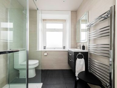 A bathroom with a shower enclosure a toilet a sink with a cabinet a mirror and a heated towel rack at Harbour View Cottage in Watchet