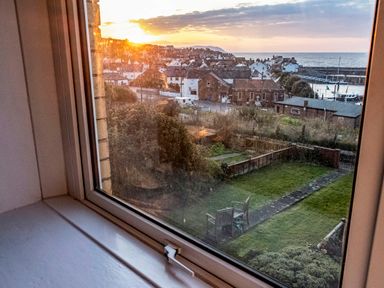 A view through a window showing a garden with a table and chairs a path a fence houses and the sea at Harbour View Cottage in Watchet