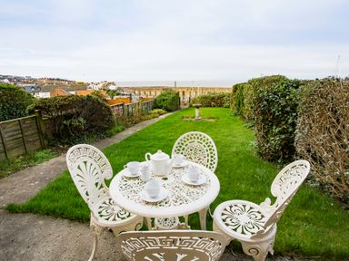 A garden with a white metal table and four chairs with a tea set on the table at Harbour View Cottage in Watchet