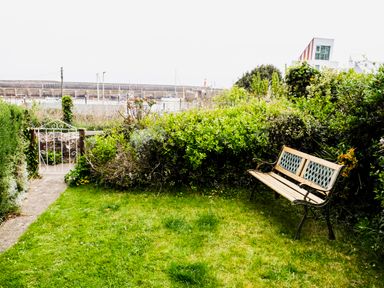 A garden with a metal bench and green bushes near a white gate at Harbour View Cottage in Watchet
