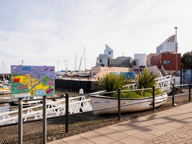 A harbour with boats docked a sign with a map and a boat planter with plants near the water at Harbour View Cottage in Watchet