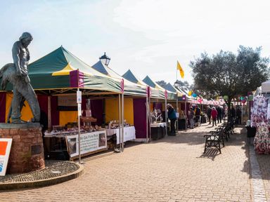 An outdoor market with tents and stalls along a walkway with a statue and benches at Harbour View Cottage in Watchet