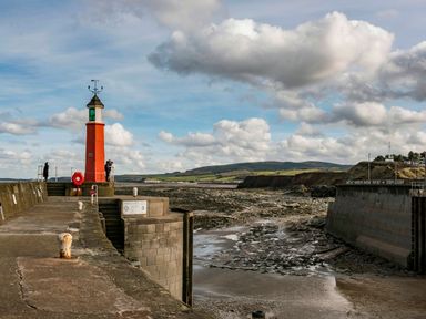 A harbor with a red lighthouse on a concrete pier and a rocky shoreline at Harbour View Cottage in Watchet