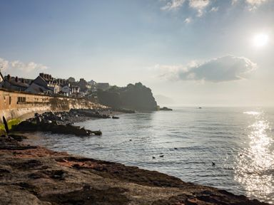 A coastline with houses along a sea wall and rocks in the water at Harbour View Cottage in Watchet