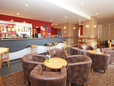 A bar area with stools and tables surrounded by armchairs at Running Waters in Callington