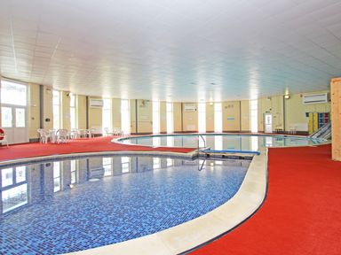 An indoor swimming pool area with a smaller pool section and white plastic chairs and tables at Running Waters in Callington