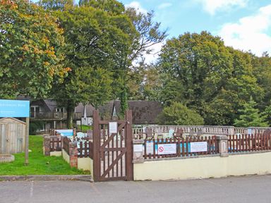 An outdoor swimming pool area with wooden gate and picket fence surrounded by trees at Running Waters in Callington