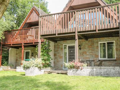 A two story stone house with a wooden balcony and outdoor seating area at Running Waters in Callington