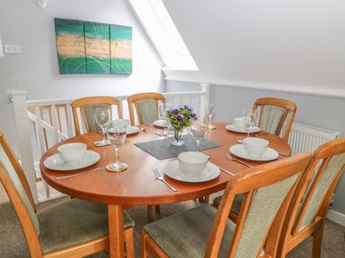 A dining room with a wooden table set for six with white dishes and glasses and a vase with flowers on the table at Running Waters in Callington