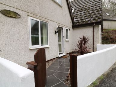 An exterior view of a house entrance with a tiled path brown gate white walls and a plant at Running Waters in Callington