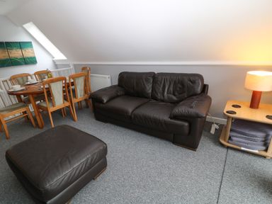 A living room with a brown leather sofa and ottoman a wooden dining table with chairs and a lamp on a side table at Running Waters in Callington