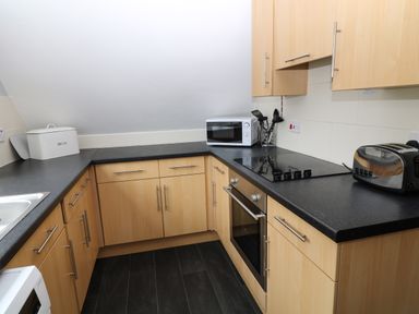 A kitchen with wooden cabinets black countertops a microwave toaster and stovetop at Running Waters in Callington