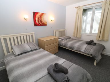 A bedroom with two single beds gray bedding a wooden chest of drawers and a window with curtains at Running Waters in Callington