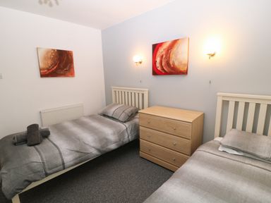 A bedroom with two single beds a wooden chest of drawers and abstract paintings on the walls at Running Waters in Callington