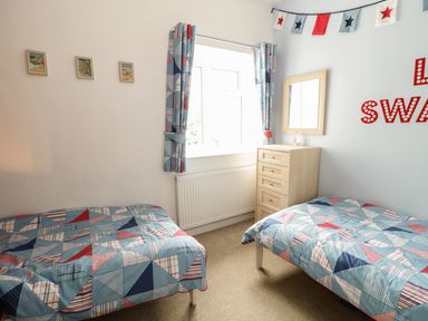 A bedroom with two single beds blue patterned bedding a wooden chest of drawers and a window with matching curtains at Swanage Bay Apartment in Swanage