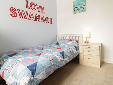 A single bed with a colorful quilt next to a wooden nightstand with a lamp and wall art above at Swanage Bay Apartment in Swanage