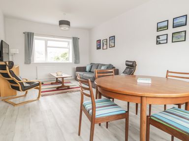 A living room with a wooden dining table and chairs a sofa two armchairs a coffee table and framed pictures on the wall at Swanage Bay Apartment in Swanage