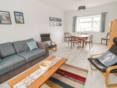 A living room with a gray sofa a wooden coffee table a black armchair with a pillow and a round dining table with chairs at Swanage Bay Apartment in Swanage