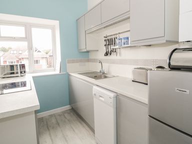 A kitchen with white cabinets a dishwasher a sink a microwave and a refrigerator at Swanage Bay Apartment in Swanage