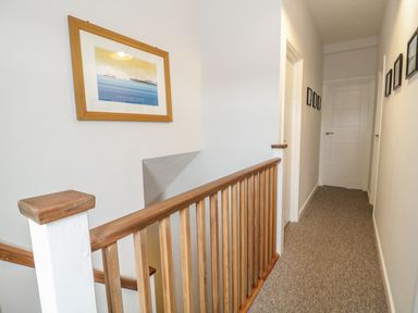 A hallway with carpet flooring, white doors, wooden railing, and framed pictures on the walls at Swanage Bay Apartment in Swanage