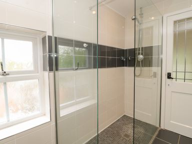 A bathroom with a glass shower enclosure a tiled shower area and a window at Red Squirrel Cottage 5 Biddlestone in Rothbury