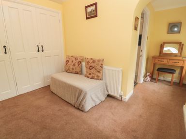 A room with a covered bench with cushions next to a radiator a wooden dressing table with a stool and a small toy in the corner at Red Squirrel Cottage 5 Biddlestone Rothbury