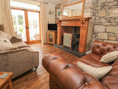 A living room with a stone fireplace a leather sofa fabric sofa wooden floor and glass doors at Red Squirrel Cottage 5 Biddlestone in Rothbury