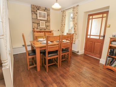 A dining room with a wooden table set for six next to a stone fireplace and a wooden door at Red Squirrel Cottage 5 Biddlestone Rothbury