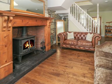 A living room with a wood burning stove fireplace leather sofa and staircase at Red Squirrel Cottage 5 Biddlestone Rothbury
