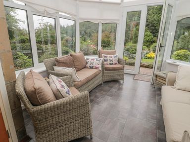A conservatory with wicker sofas and butterfly cushions overlooking a garden at Red Squirrel Cottage 5 Biddlestone in Rothbury