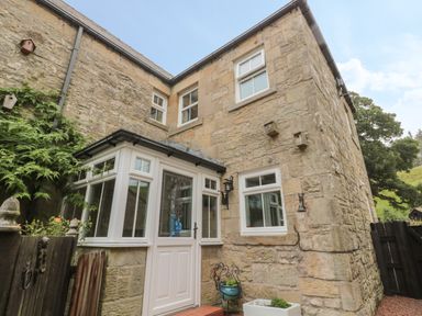 The exterior of a stone house with white framed windows and a white door with glass panels at Red Squirrel Cottage 5 Biddlestone in Rothbury
