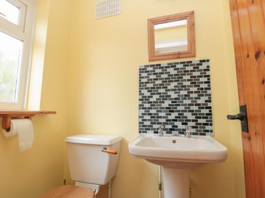 A small bathroom with a toilet and a sink under a tiled backsplash and a wooden mirror with a window and wooden door at Red Squirrel Cottage 5 Biddlestone Rothbury