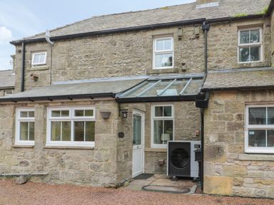 The exterior of a stone house with multiple windows a white door a glass porch roof and an outdoor air conditioning unit at Red Squirrel Cottage 5 Biddlestone in Rothbury