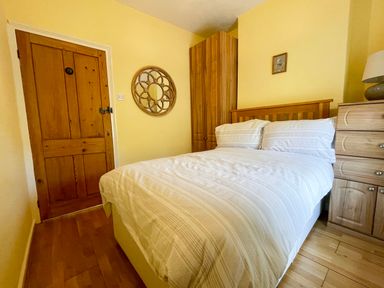 A bedroom with a double bed a wooden door a round wall mirror a wooden corner wardrobe and a wooden chest of drawers at Red Squirrel Cottage 5 Biddlestone in Rothbury
