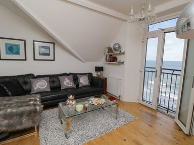 A living room with a black sofa and decorative pillows a glass coffee table with ornaments a chandelier and a sea view at Flat 3 Peacehaven Sandsend near Whitby