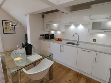 A kitchen with white cabinets a glass dining table with white chairs and a floor lamp at Flat 3 Peacehaven Sandsend near Whitby