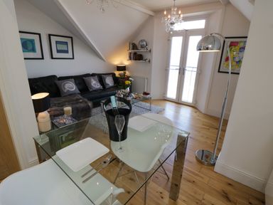 A living room with a glass dining table a black leather sofa and double doors at Flat 3 Peacehaven Sandsend near Whitby