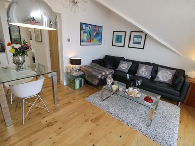 A living room with a black sofa a glass coffee table and a glass dining table at Flat 3 Peacehaven Sandsend near Whitby