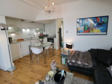 A kitchen and living area with white cabinets glass table and chairs a black sofa with a fur throw at Flat 3 Peacehaven Sandsend near Whitby