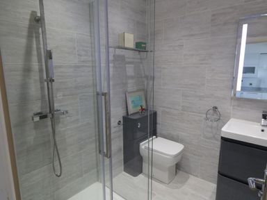 A bathroom with a glass shower enclosure a toilet a sink with a cabinet and a lit mirror at Flat 3 Peacehaven Sandsend near Whitby