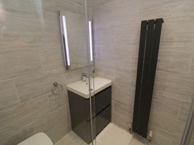 A bathroom with a sink and cabinet a mirror with lights a vertical radiator and a white rug at Flat 3 Peacehaven Sandsend near Whitby