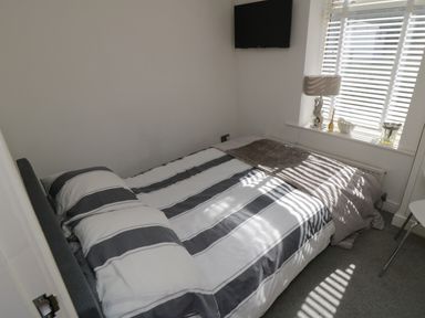 A bedroom with a bed striped bedding a wall-mounted TV and a window with blinds at Flat 3 Peacehaven Sandsend near Whitby