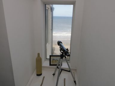 A telescope on a tripod in front of a window with a view of the sea a framed picture and a decorative bottle on the window ledge at Flat 3 Peacehaven Sandsend near Whitby