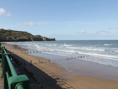 A beach with waves and wooden groynes with cliffs and green railings at Flat 3 Peacehaven in Sandsend near Whitby