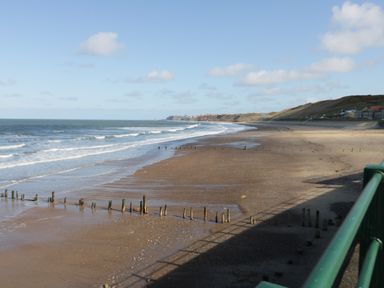 A beach with wooden posts running into the sea and houses on the hill at Flat 3 Peacehaven Sandsend near Whitby